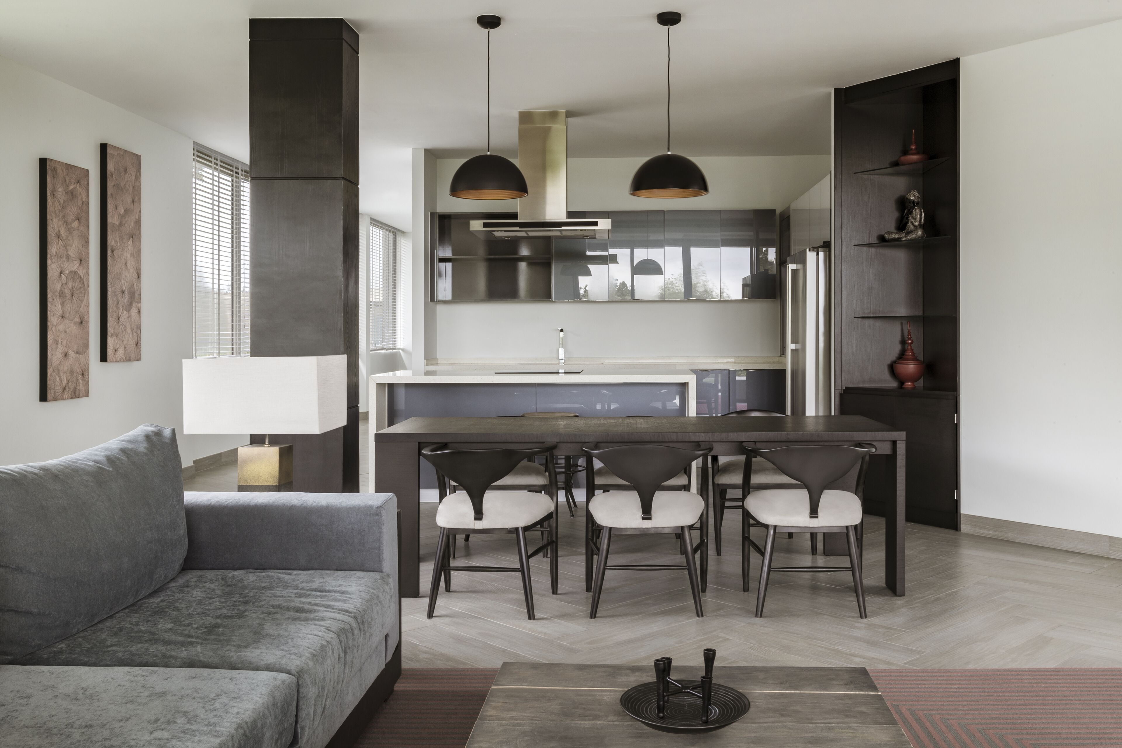 A modern kitchen with a central island, pendant lighting, and a dining area with chairs.