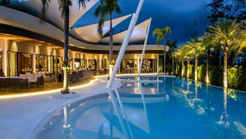 A modern hotel with a pool, palm trees, and a well-lit outdoor area.