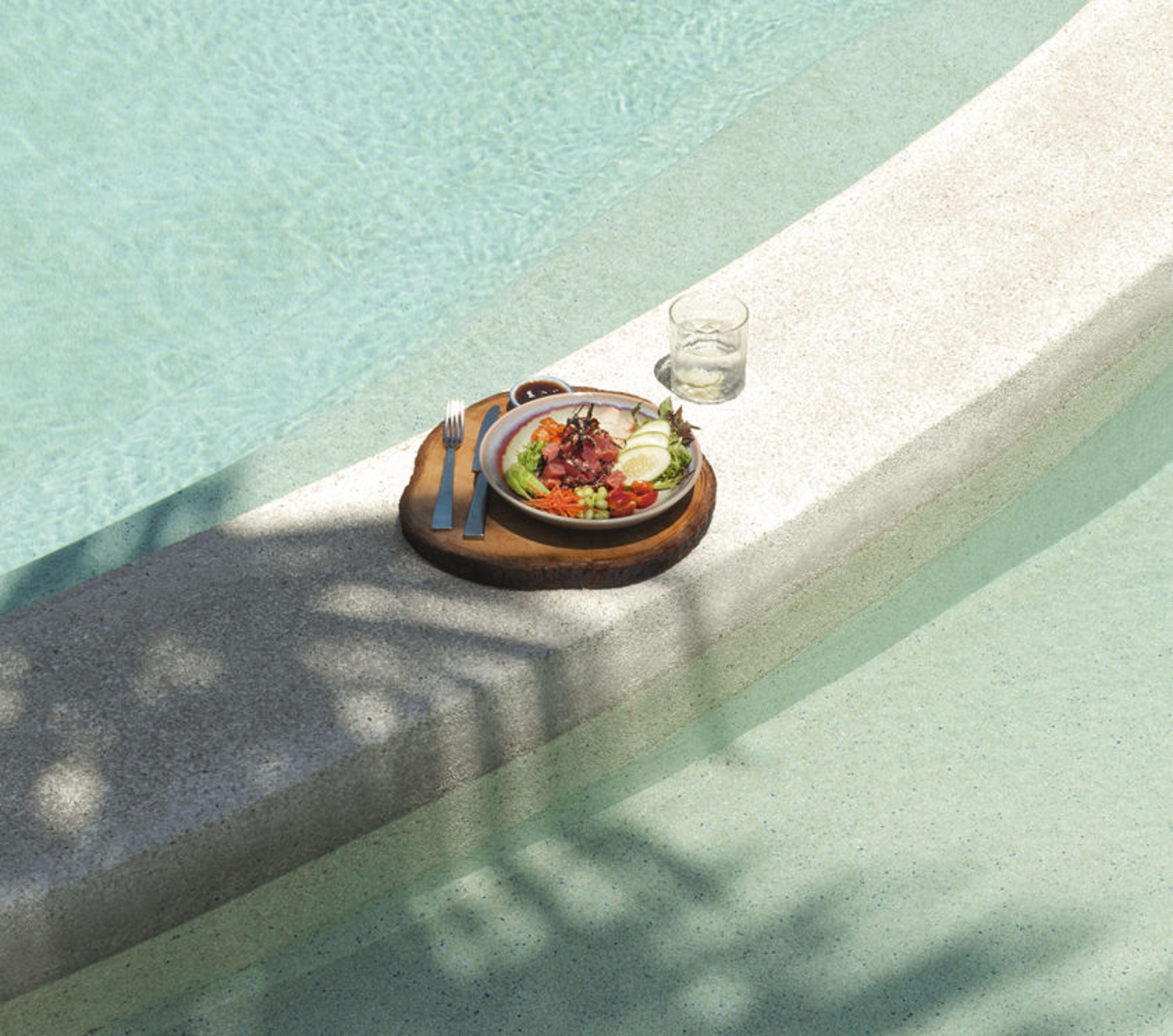 A dining table with a meal and cutlery by a poolside.