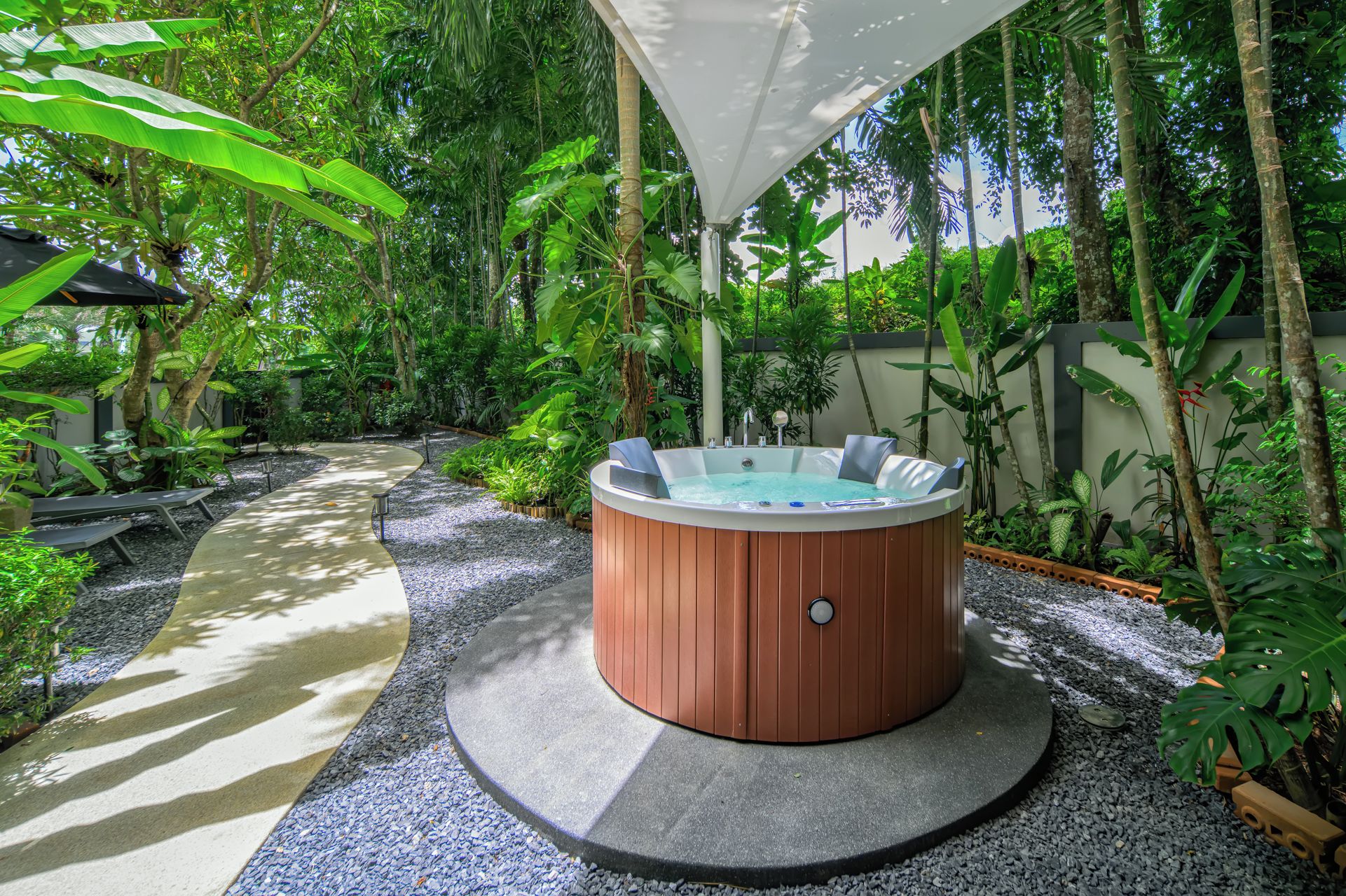 A hot tub surrounded by a garden with a pathway leading to it.