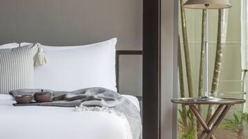 Une chambre à coucher avec un lit, une table de chevet, une lampe et une vue sur des bambous, visible à travers une porte vitrée.