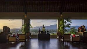 A spacious room with a large window offering a view of mountains and a cityscape. There are several chairs and a sofa arranged for seating. - The Pavilions Phuket (Choeng Thale)