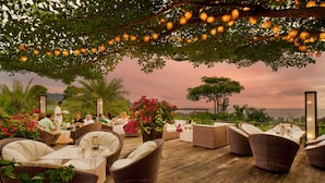 An outdoor seating area with wicker furniture, a table, and a view of the ocean at sunset. - The Pavilions Phuket (Choeng Thale)