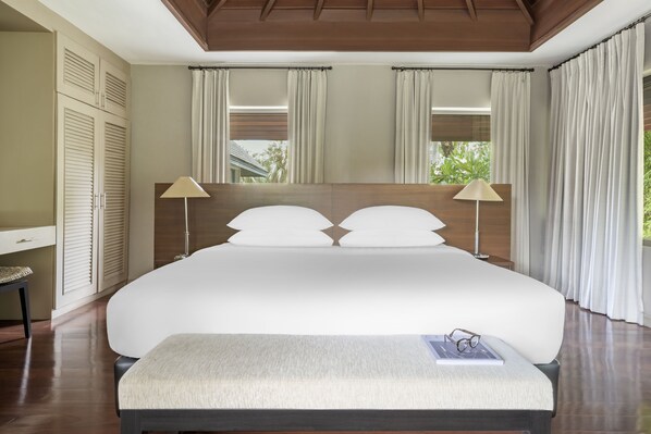 A large bed with a headboard, two bedside lamps, and a bench with a book and glasses.