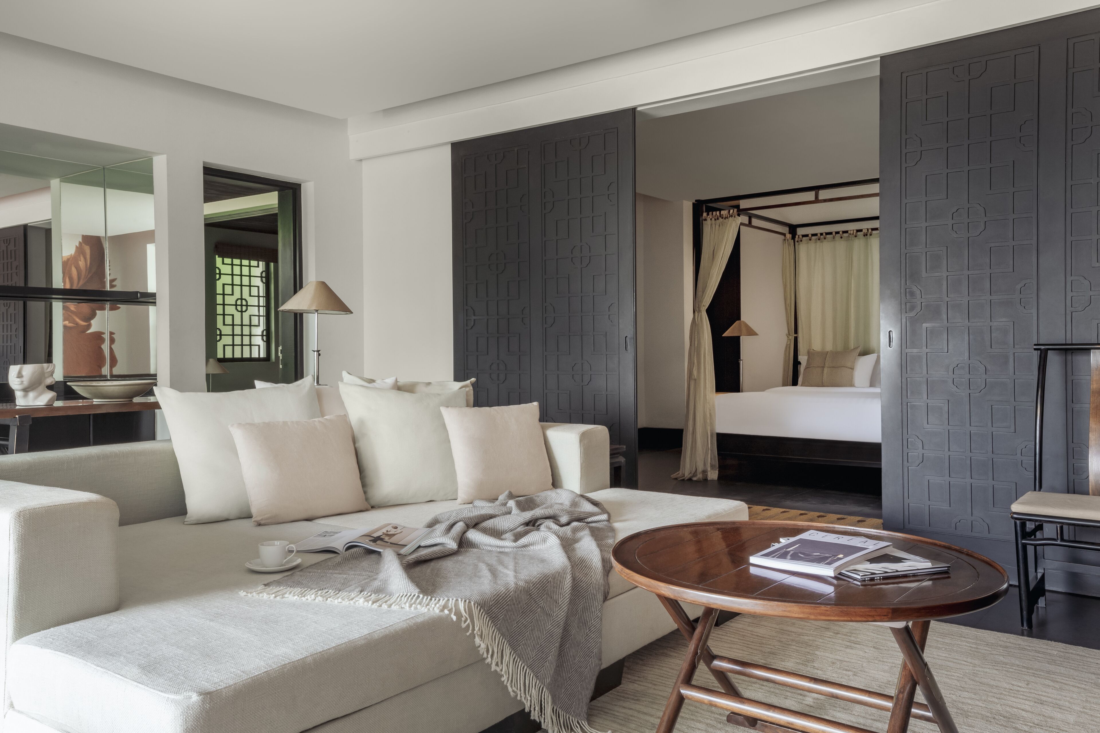 Une chambre d’hôtel moderne avec un canapé, une table ronde en bois et un lit à baldaquin.
