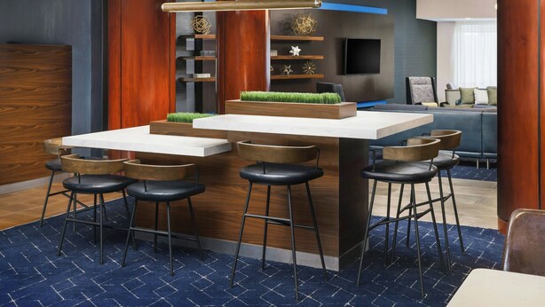 A modern bar area with a central island, bar stools, and a flat-screen TV mounted on the wall. - Courtyard By Marriott Farmington (Newington)