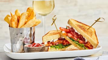 Um prato com um sanduíche grelhado, um copo de vinho branco e um recipiente com batatas fritas.