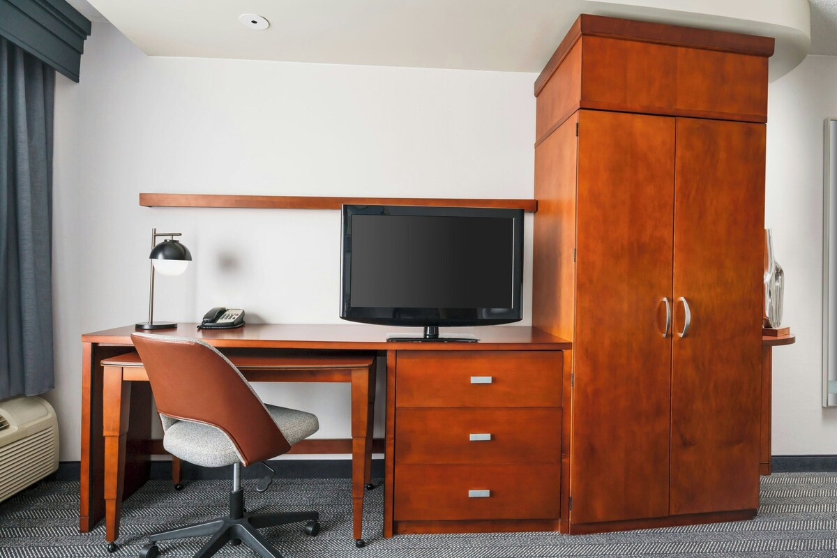 A hotel room with a wooden desk, a television, a chair, and a wardrobe.
