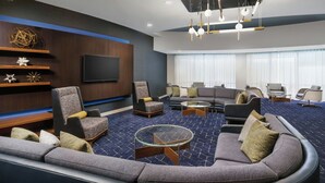 A modern hotel lobby with a large seating area, a flat-screen TV, and a ceiling light fixture. - Courtyard By Marriott Farmington (Newington)