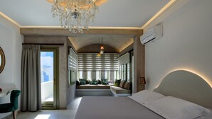 A modern bedroom with a large bed, a seating area with a view, and a chandelier. - Hotel Zephyros (Santorini)