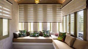 A modern interior with a built-in bench and sofa, large windows with blinds, and pendant lighting. - Hotel Zephyros (Santorini)