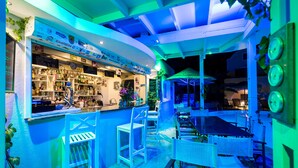 A bar area with seating and a counter, surrounded by greenery and a blue-lit ceiling. - Hotel Zephyros (Santorini)