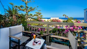 A balcony with wicker chairs and a table, overlooking a coastal view with a clear sky. - Hotel Zephyros (Santorini)