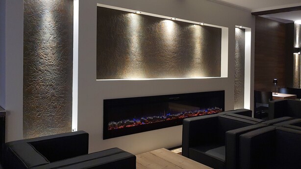 Un área de descanso moderna con asientos de cuero negro, una mesa de madera y un televisor de pared mostrando un paisaje urbano.
