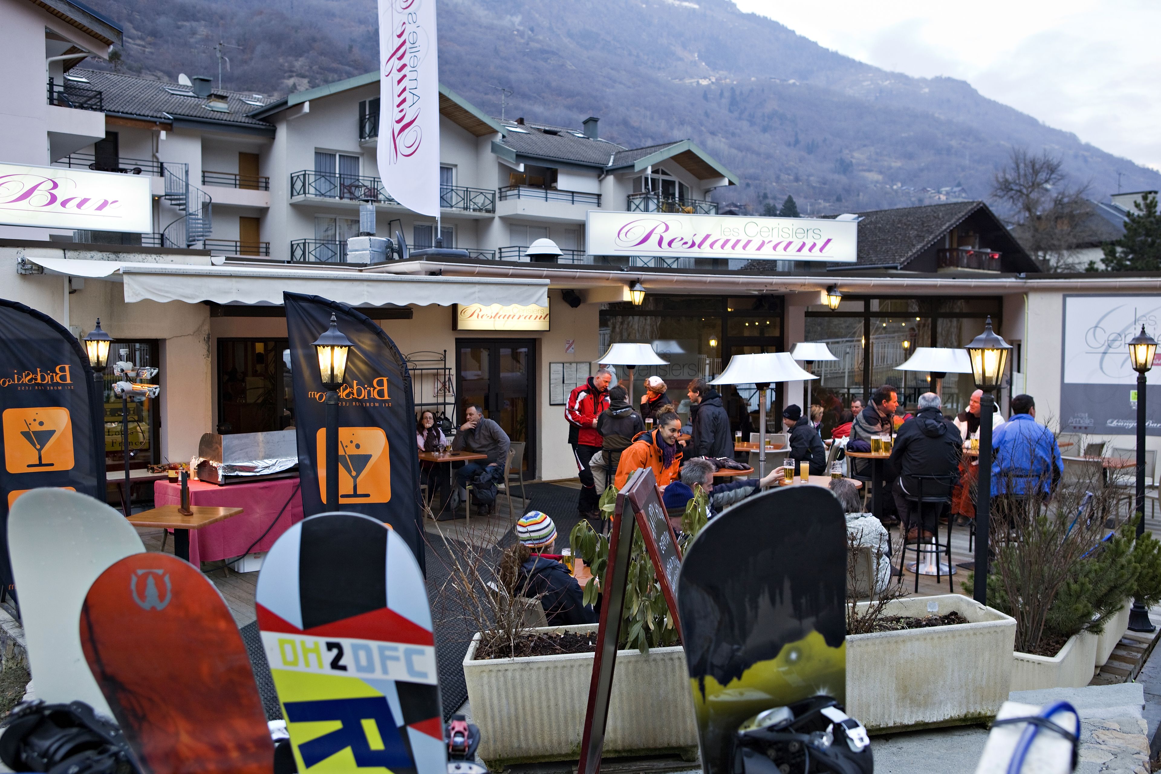 Un restaurant avec une terrasse, une vue sur les montagnes en arrière-plan et des planches de snowboard au premier plan.