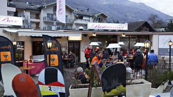 Un restaurante con terraza, un telón de fondo montañoso y tablas de snowboard al frente.