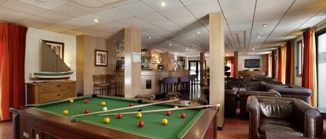 Une table de billard dans une pièce qui comprend un bar et des sièges en cuir.