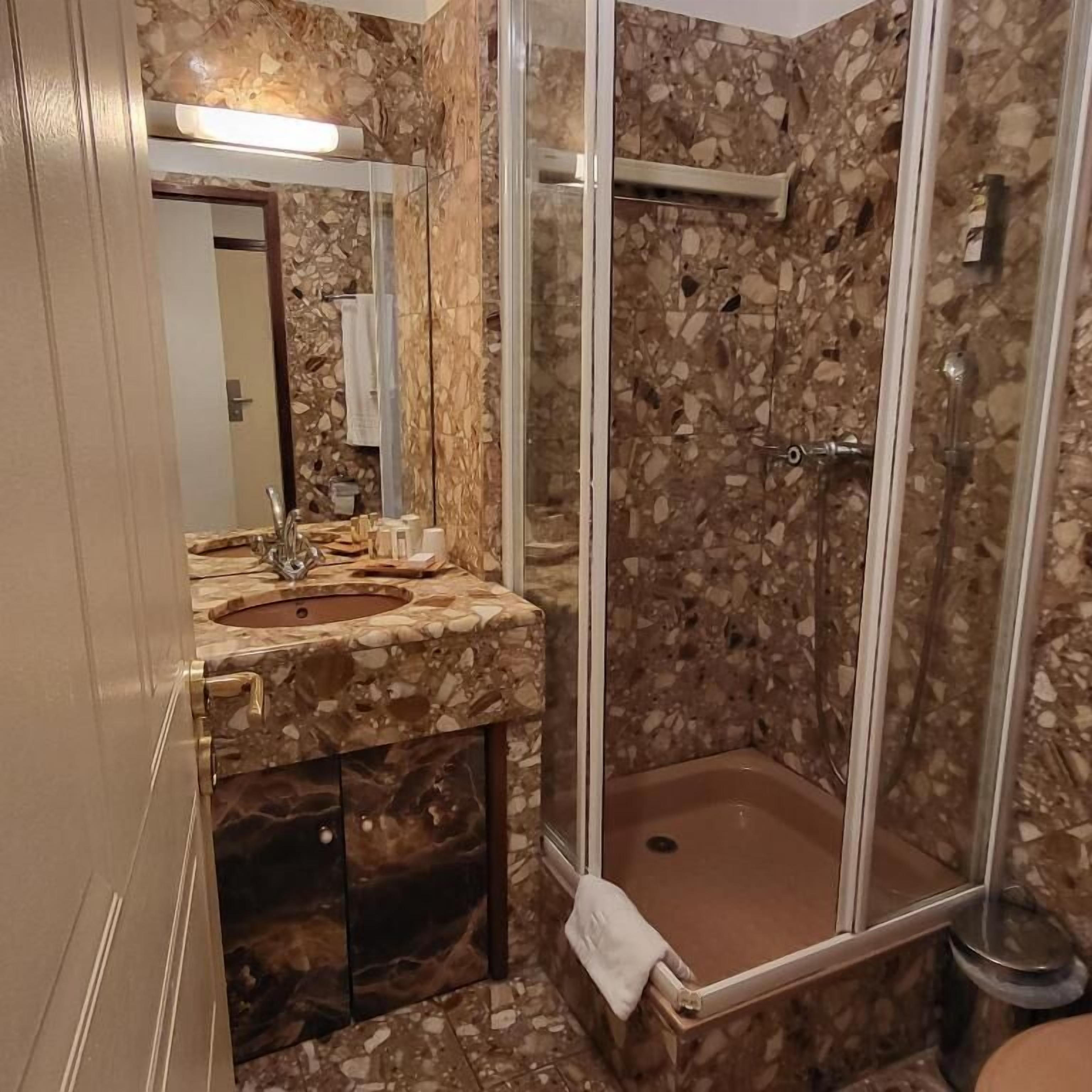 Un bagno con un lavandino in marmo, una cabina doccia in vetro e uno specchio.