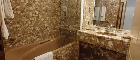 Un baño con piso de mármol, una bañera, una ducha y un lavamanos con un espejo grande.