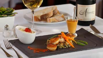 Une table à manger avec une assiette de nourriture, un verre de vin blanc et une bouteille de vin.