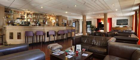 Eine Bar mit Theke, Barhocker und einer Sitzecke mit Sofas und einem Couchtisch.