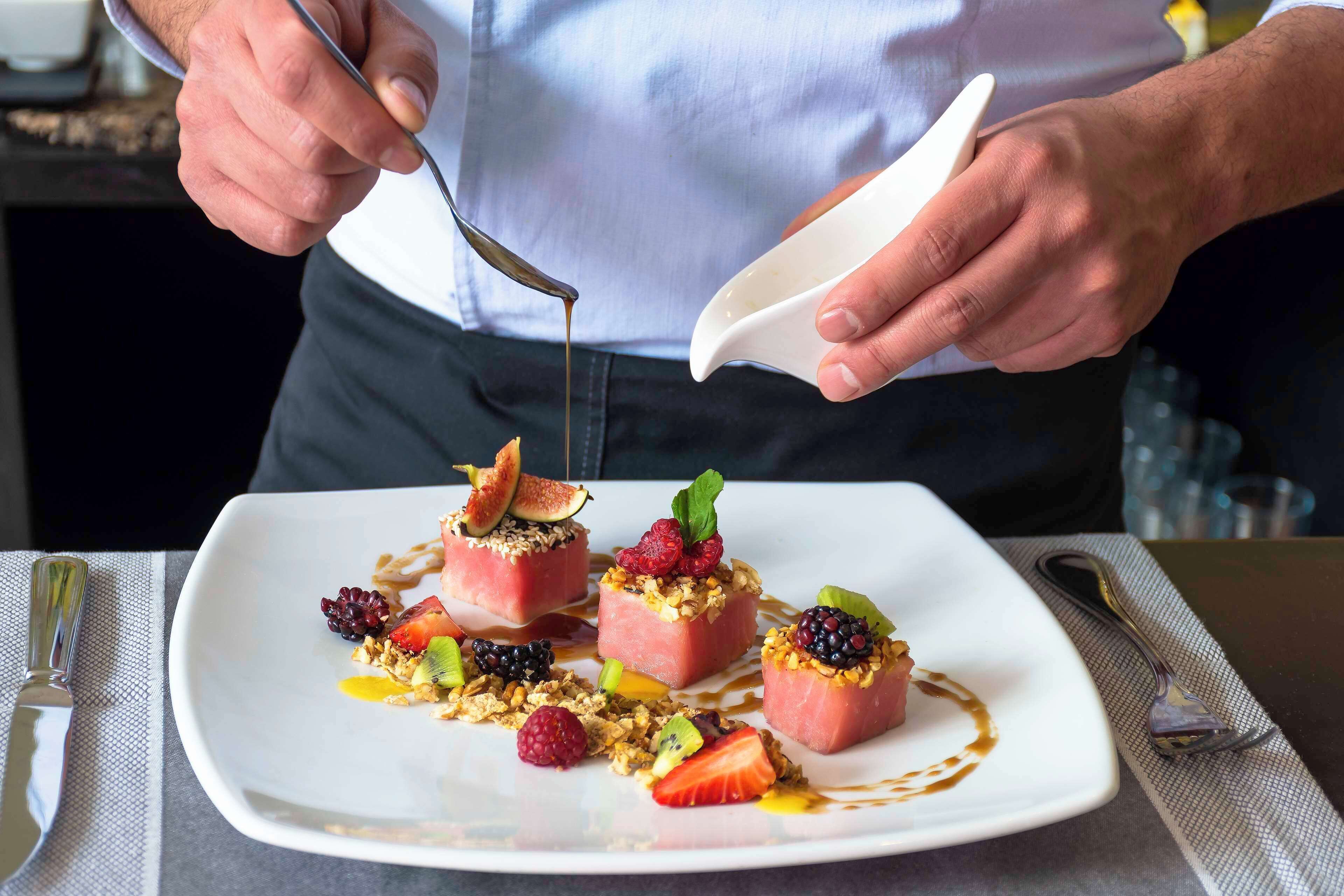 Una persona sirve un postre en un plato blanco con frutas y granola.