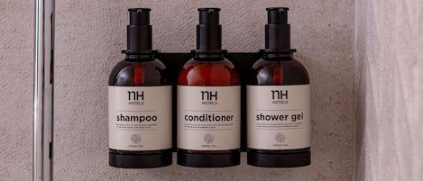Tres botellas de artículos de baño de hotel (champú, acondicionador, gel de ducha) en una pared.