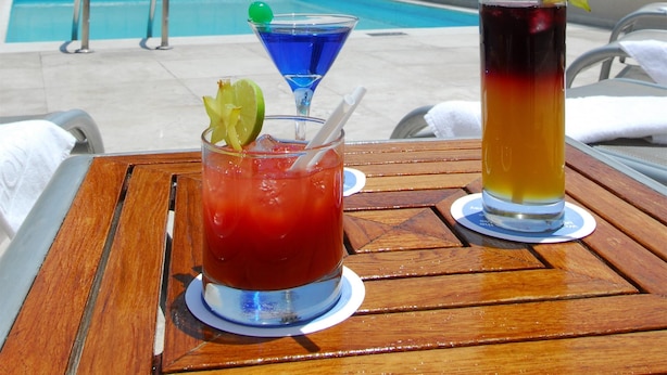 A poolside table with two drinks, a pool, and a building with a dome in the background. - NH Puebla Centro Histórico (Puebla)
