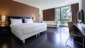 A modern hotel room with a large bed, a sofa, a desk, and a TV. - NH Puebla Centro Histórico (Puebla)