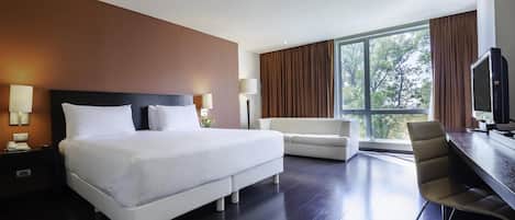 A modern hotel room with a large bed, a sofa, a desk, and a TV.