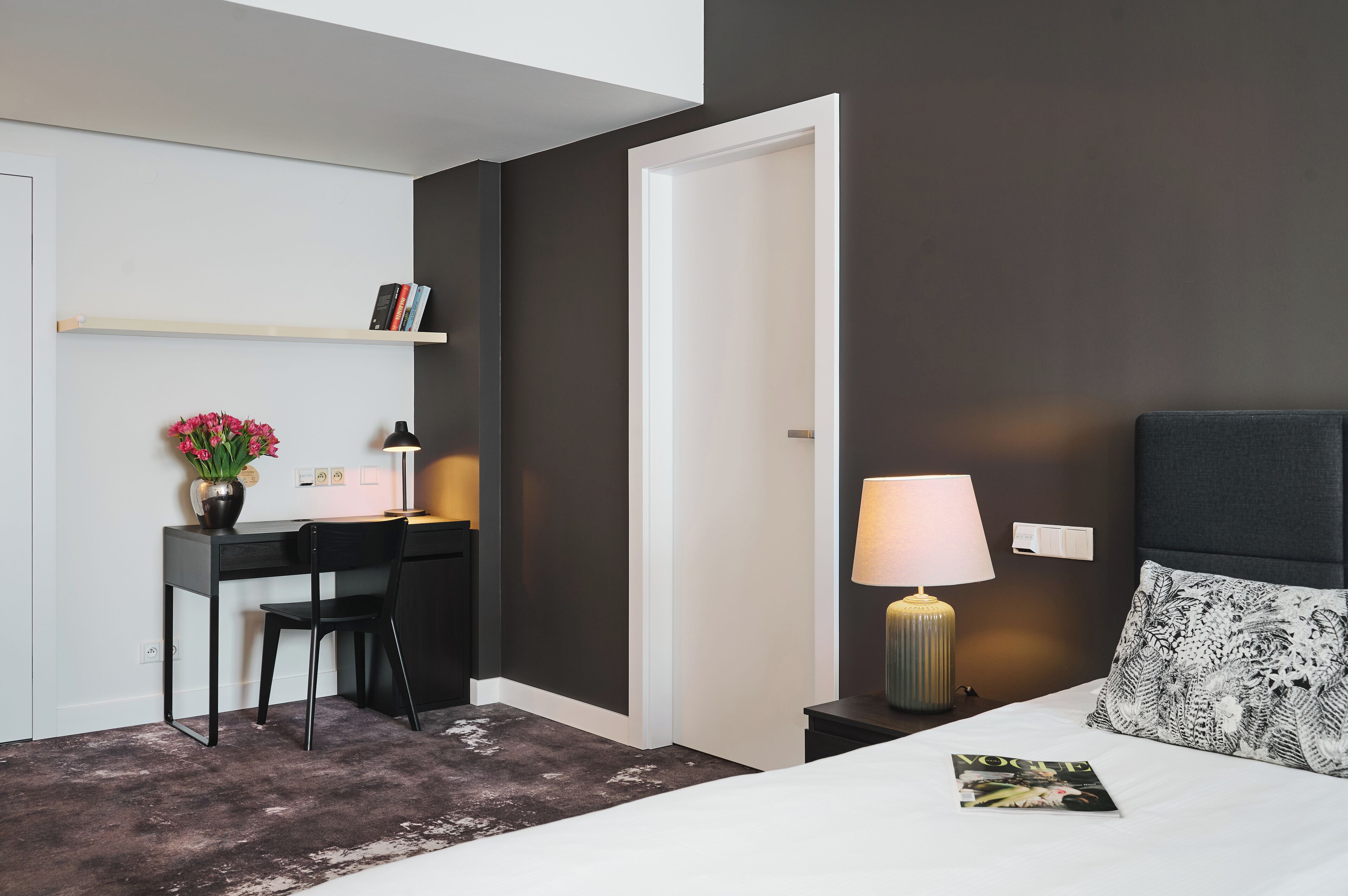 A hotel room with a desk, chair, and a bed with a pillow.