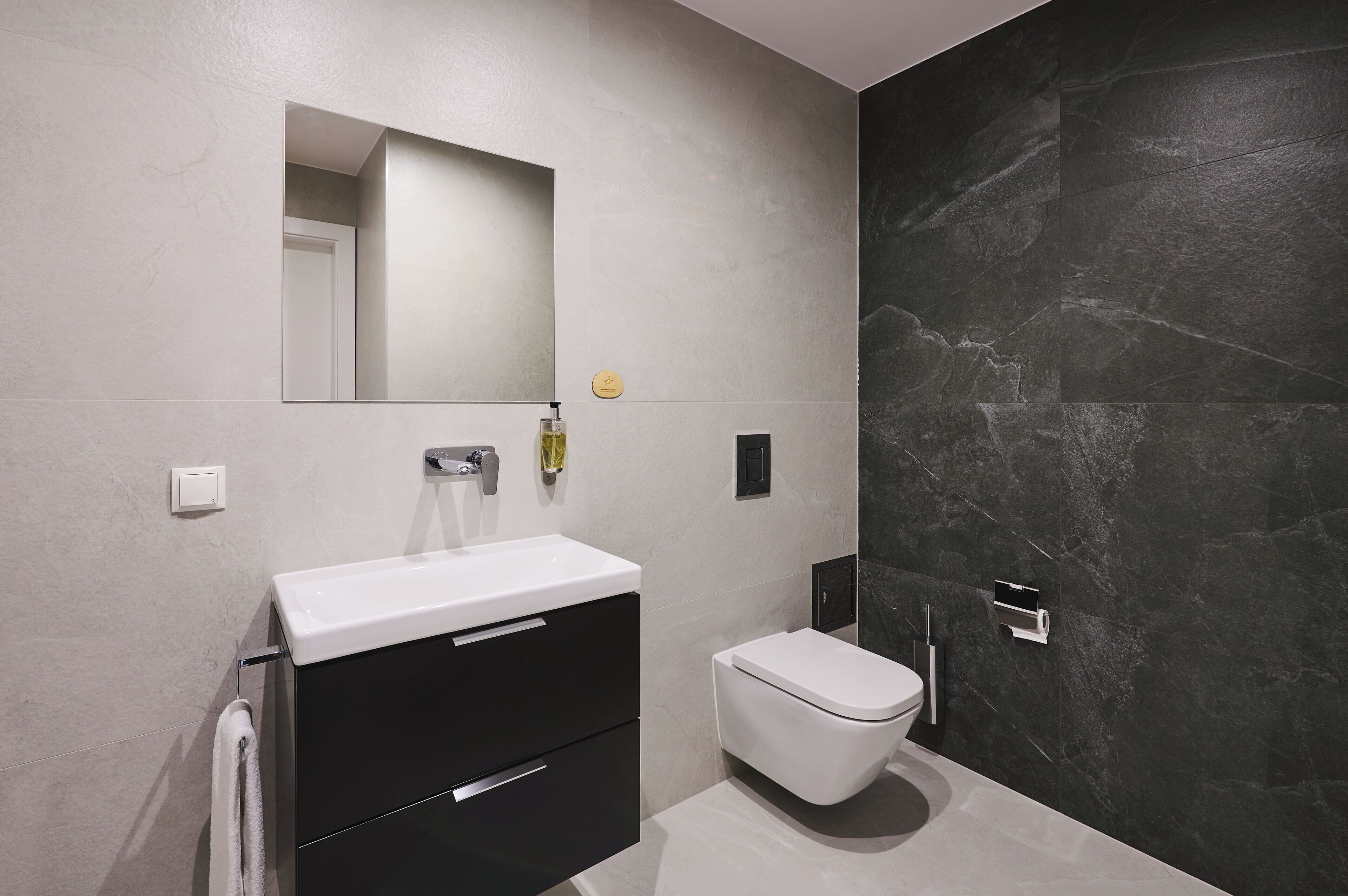 Une salle de bain moderne avec un lavabo blanc, un meuble noir et des toilettes blanches.
