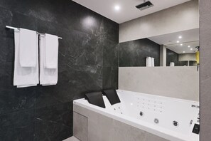Un baño moderno con una bañera grande, paredes de mármol oscuro y un espejo que refleja la habitación.