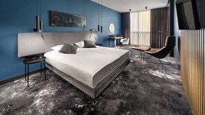 A modern hotel room with a large bed, a desk, a chair, a TV, and a cityscape painting on the wall. - Mamaison Residence Diana (Warsaw)