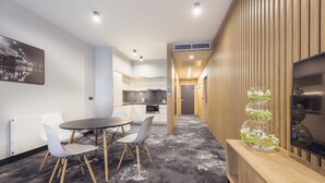 A modern kitchen with white cabinets and stainless steel appliances, a dining area with a round table and chairs, and a wooden accent wall with a decorative glass vase. - Mamaison Residence Diana (Warsaw)