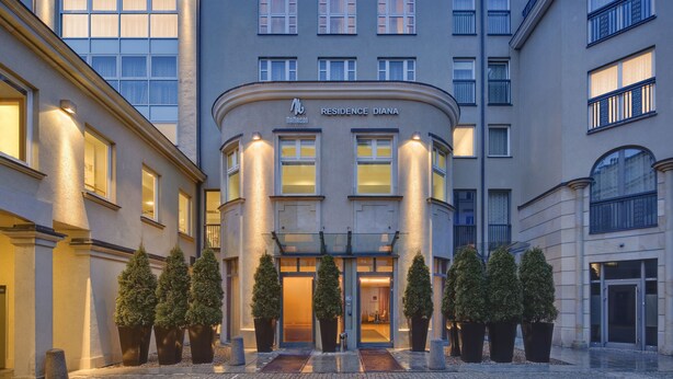 A modern hotel with a curved facade, multiple windows, and a prominent entrance with potted trees. - Mamaison Residence Diana (Warsaw)