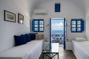 A room with a bed, a sofa, a glass table, and a view of the sea. - Heliotopos Hotel (Santorini)