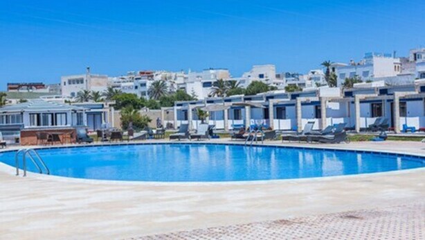 A swimming pool with lounge chairs and a row of buildings in the background. - Hotel Des Iles (Essaouira)