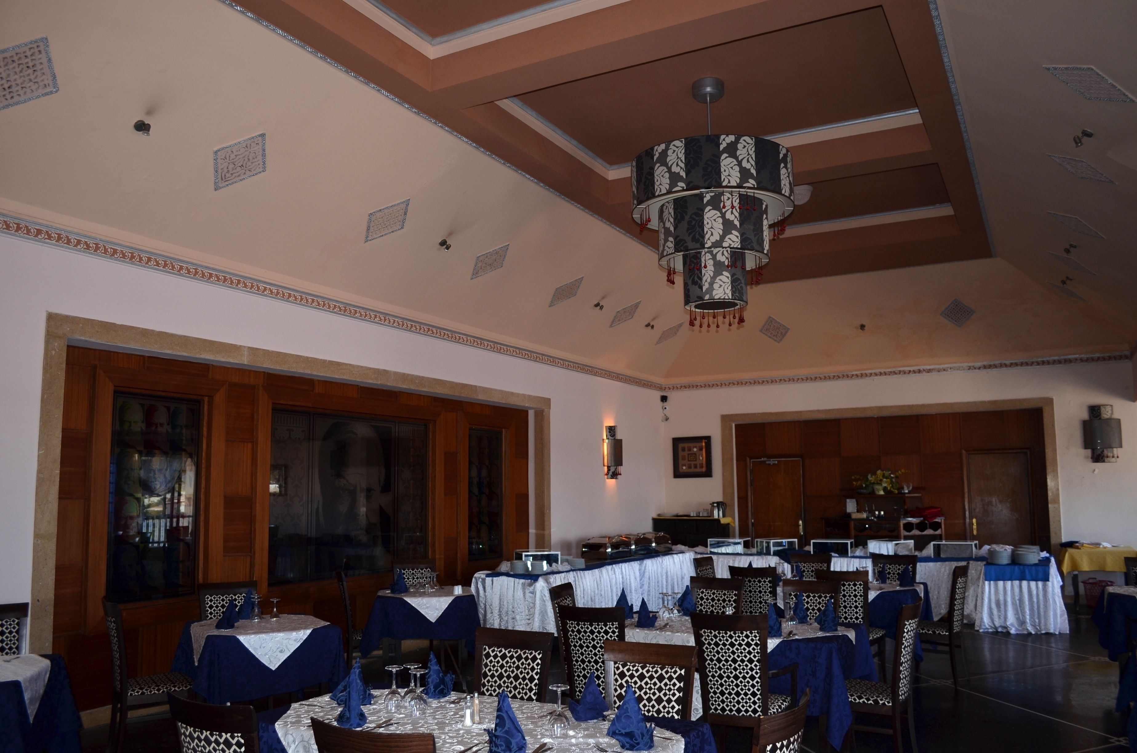 A dining area with tables set for service, a chandelier, and a kitchen in the background.