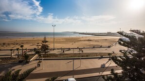 A beachside promenade with a clear view of the ocean, a paved walkway, and palm trees. - Hotel Des Iles (Essaouira)