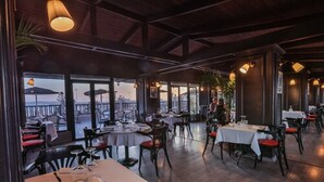 An indoor dining area with tables and chairs, large windows, and a view of the outside. - Hotel Des Iles (Essaouira)