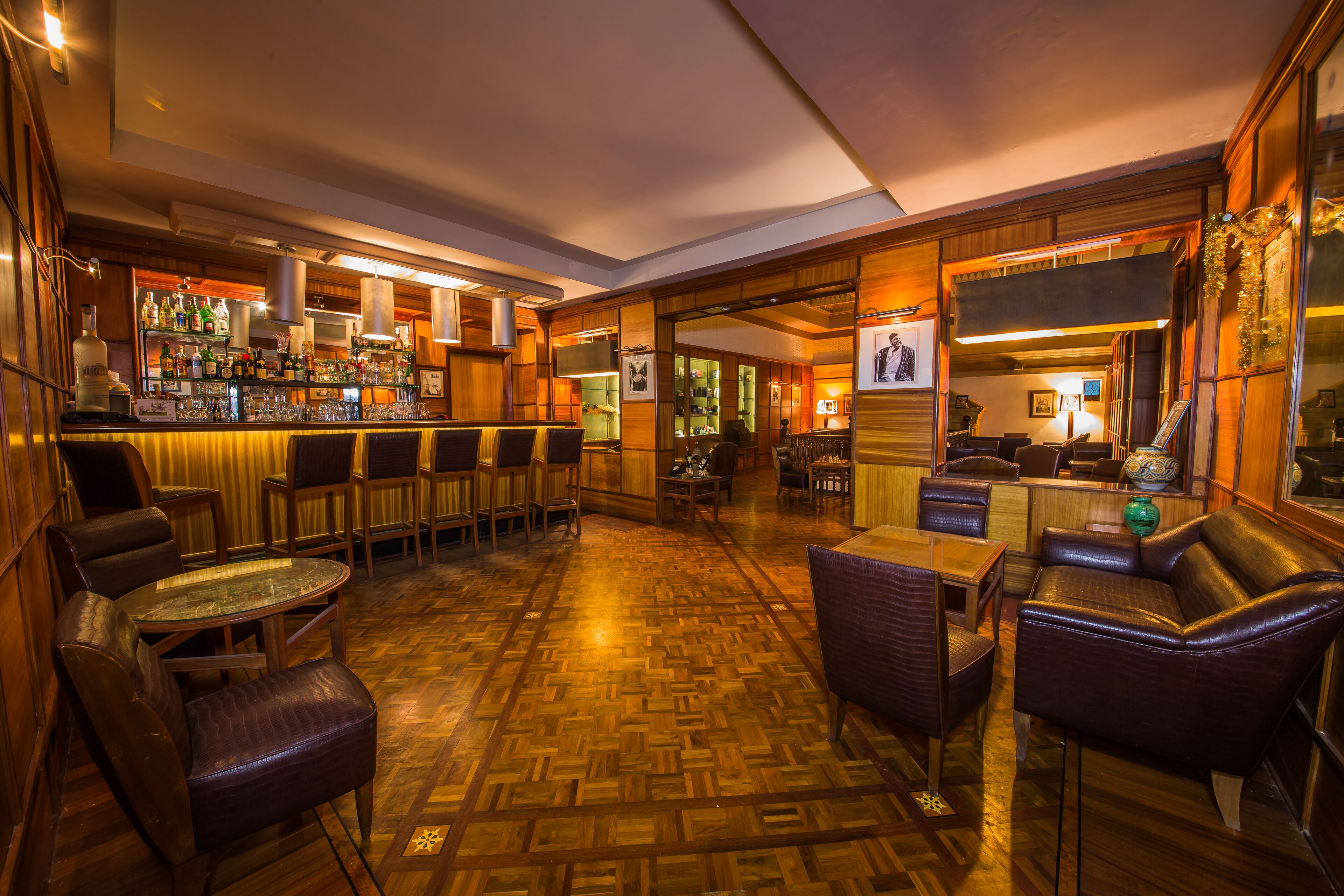 A bar area with wooden furniture, a polished parquet floor, and a variety of bottles and glasses on the shelves.