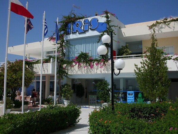 A building with the sign "IRIO" and flags, surrounded by greenery and outdoor seating. - Hotel Iris (Rhodes)
