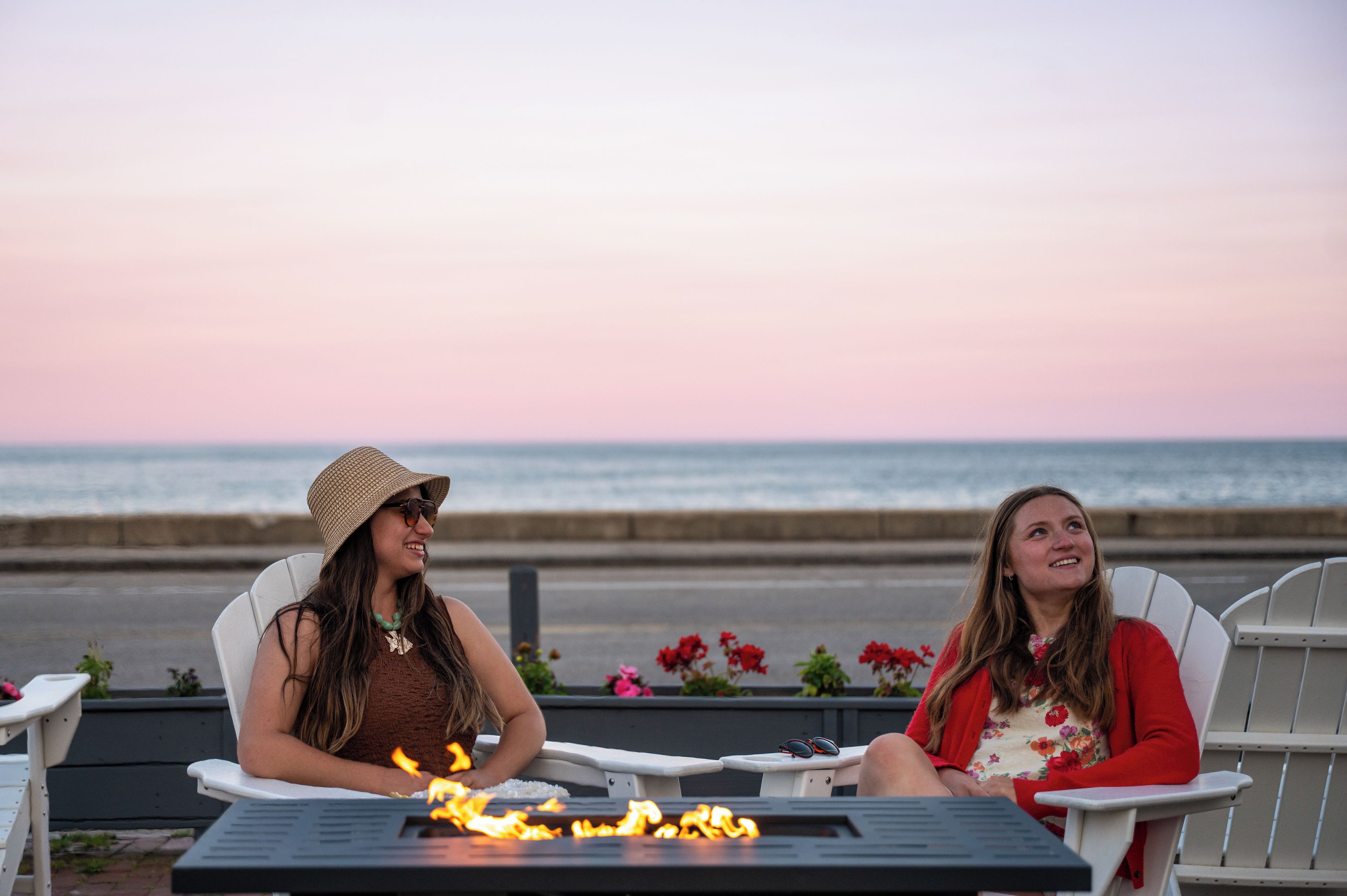 Dos personas sentadas en una mesa frente a una chimenea, con vistas a un cuerpo de agua.