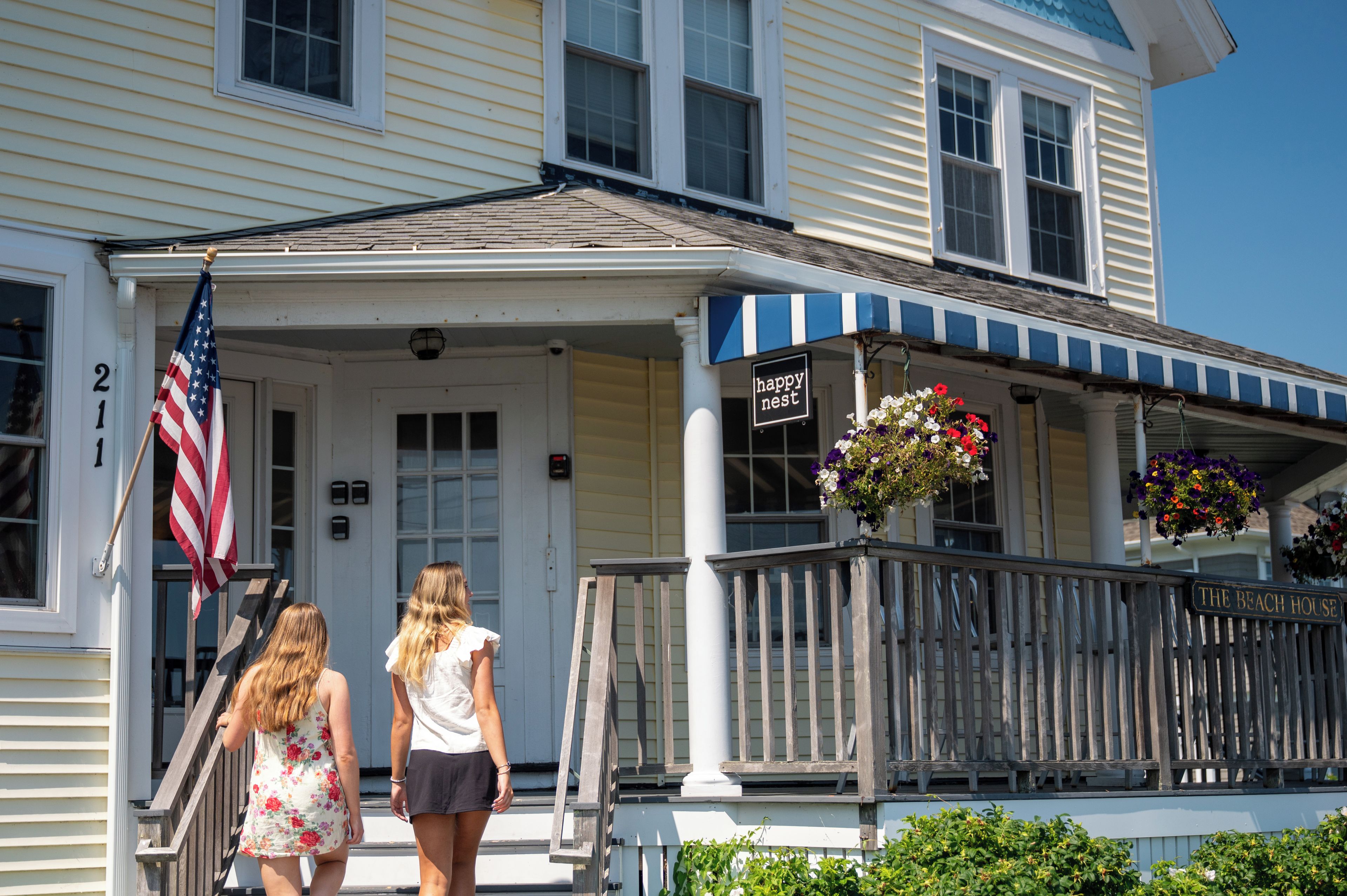 A two-story building with a porch, a flag, and a sign that reads 'happy nest.'