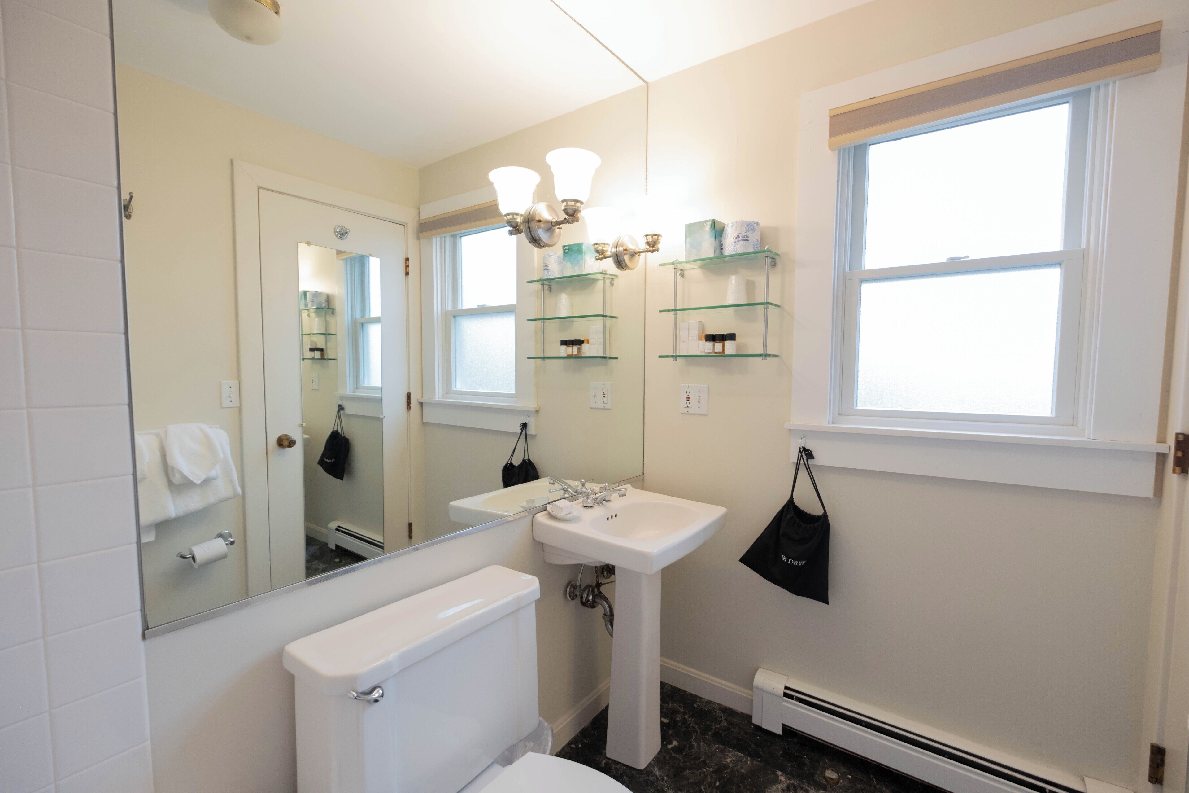 A bathroom with a toilet, sink, mirror, and shelves with toiletries.