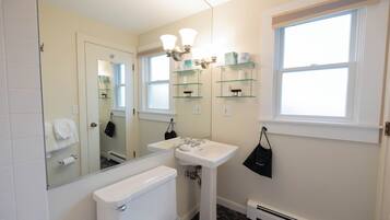 A bathroom with a toilet, sink, mirror, and shelves with toiletries.