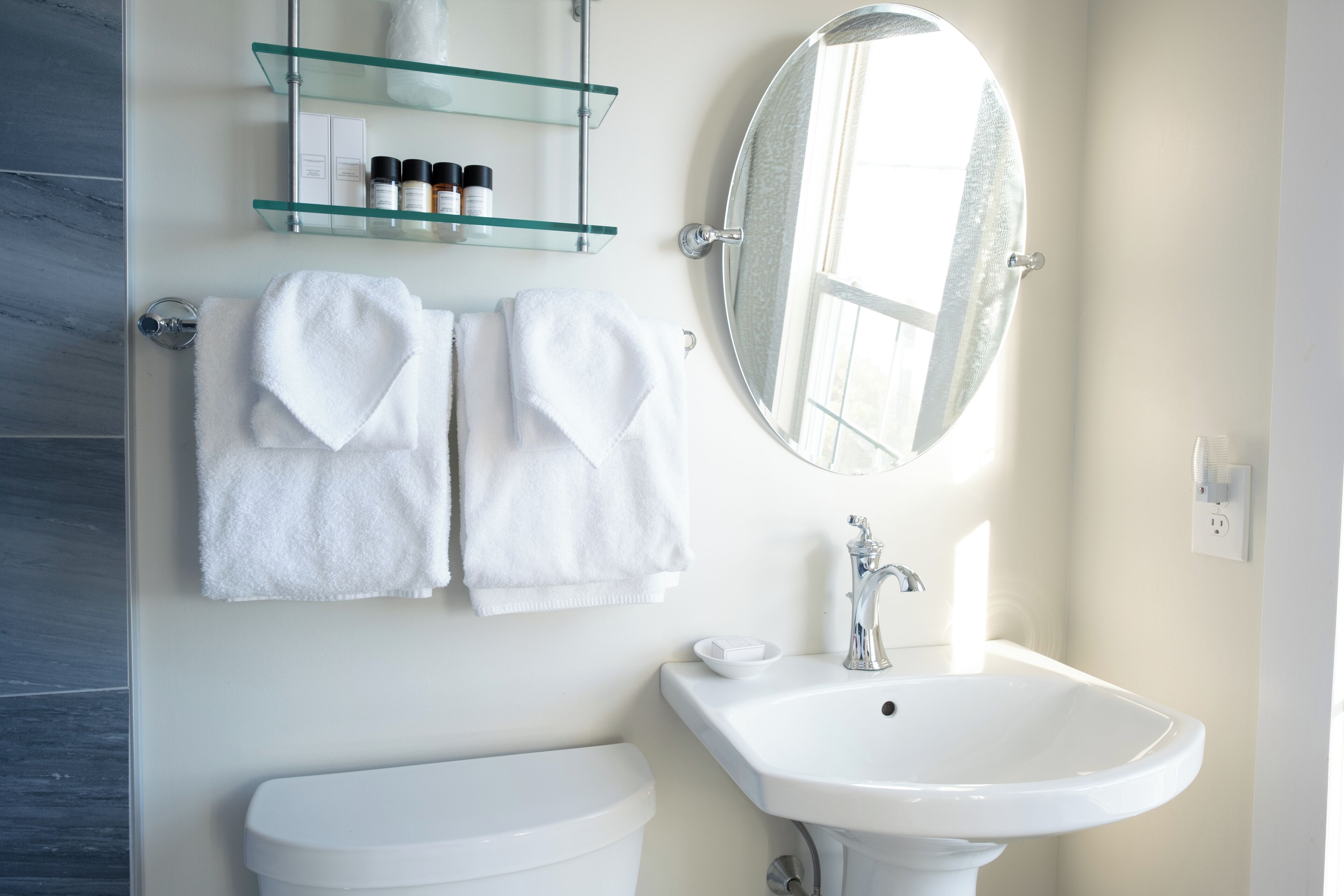 Une salle de bain avec un lavabo blanc, un miroir et deux serviettes blanches accrochées au mur.