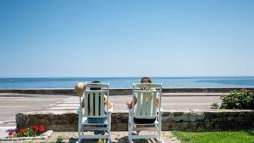 Two white chairs facing a body of water, with a clear sky above.