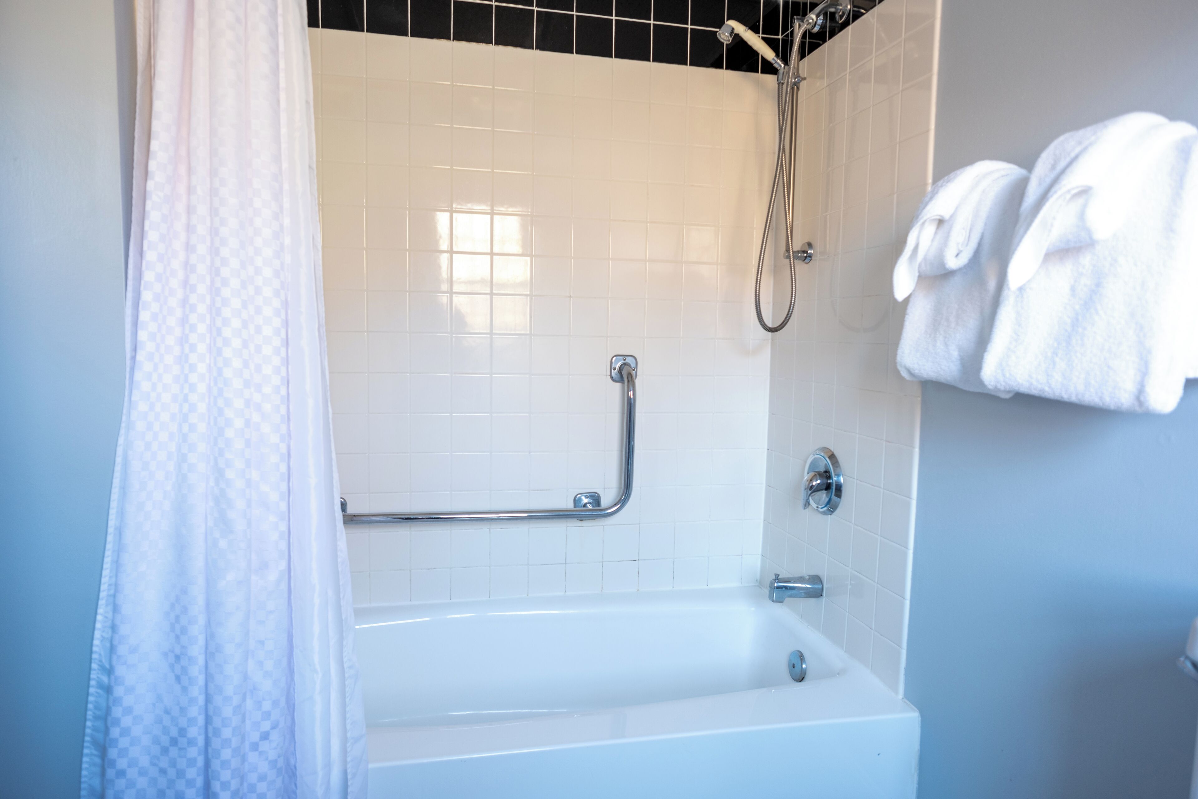 Un bagno con una vasca da bagno bianca, una doccia dotata di mancorrente e un porta asciugamani con asciugamani.